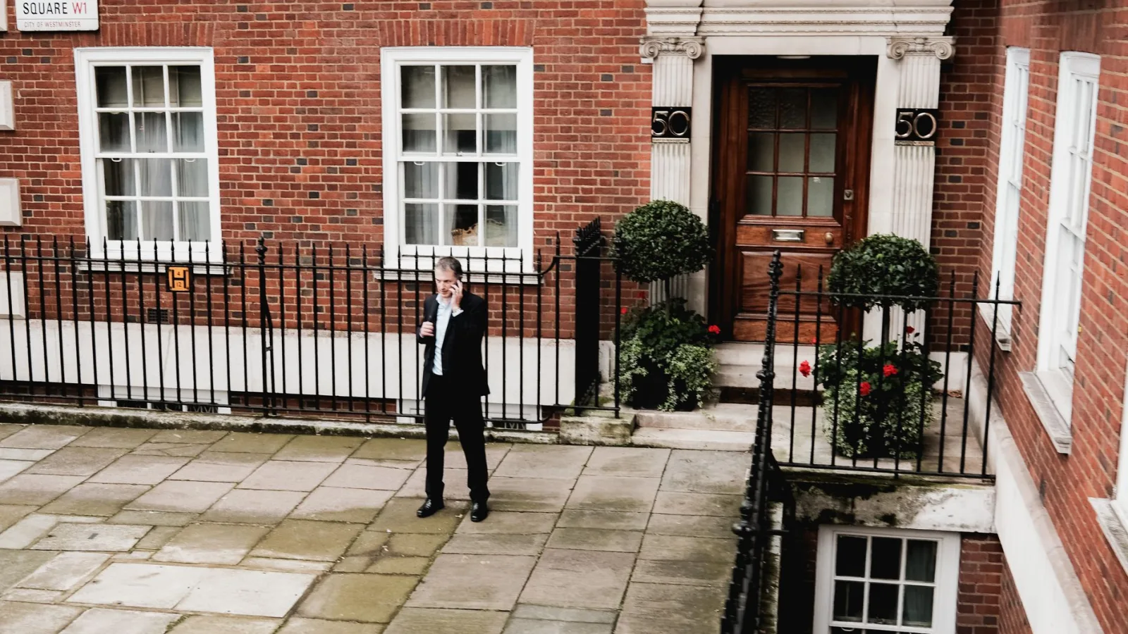 Man on phone near brick building in Grosvenor Square, London.