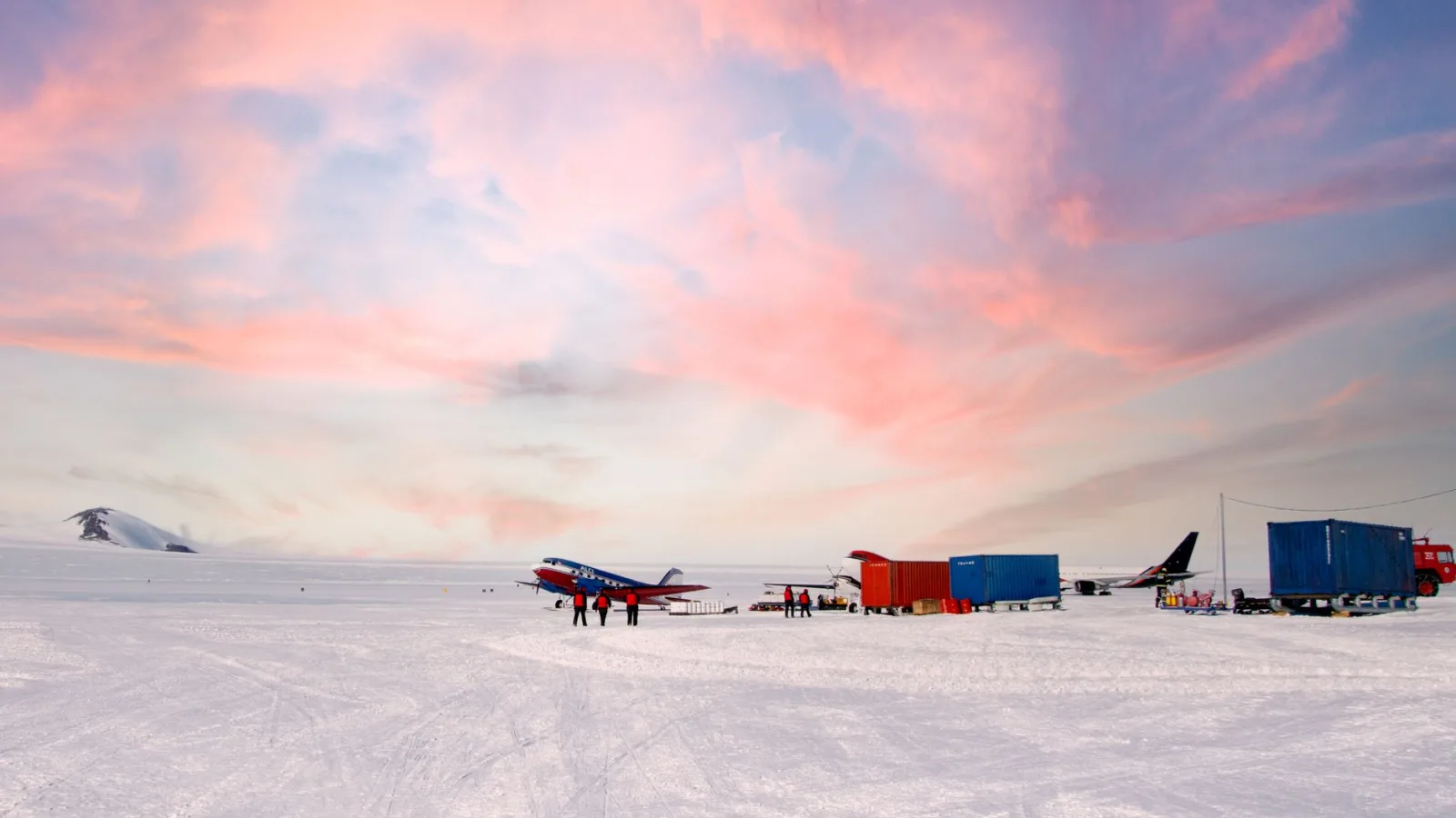 Stunning view of an Antarctic airstrip with colorful aircraft at sunset, showcasing adventure and exploration.