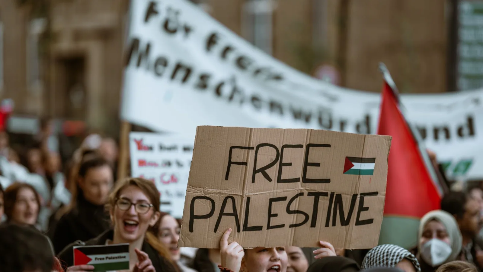 A large crowd gathers in a city for a protest holding a Free Palestine sign.