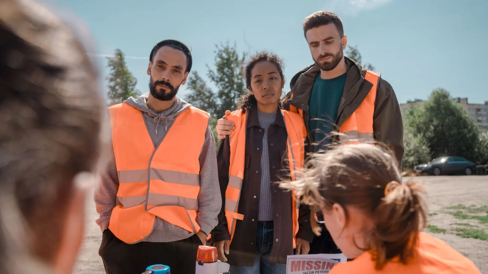 Group of volunteers wearing orange vests coordinating efforts outdoors on a sunny day.