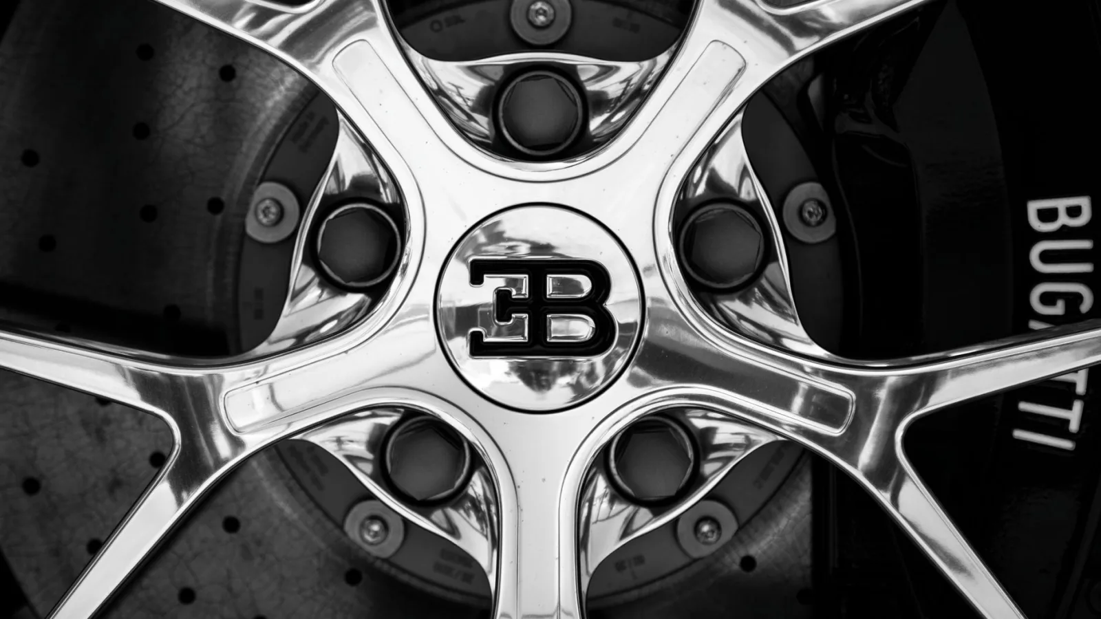 Black and white close-up shot of a Bugatti car rim showing intricate design and luxury branding.