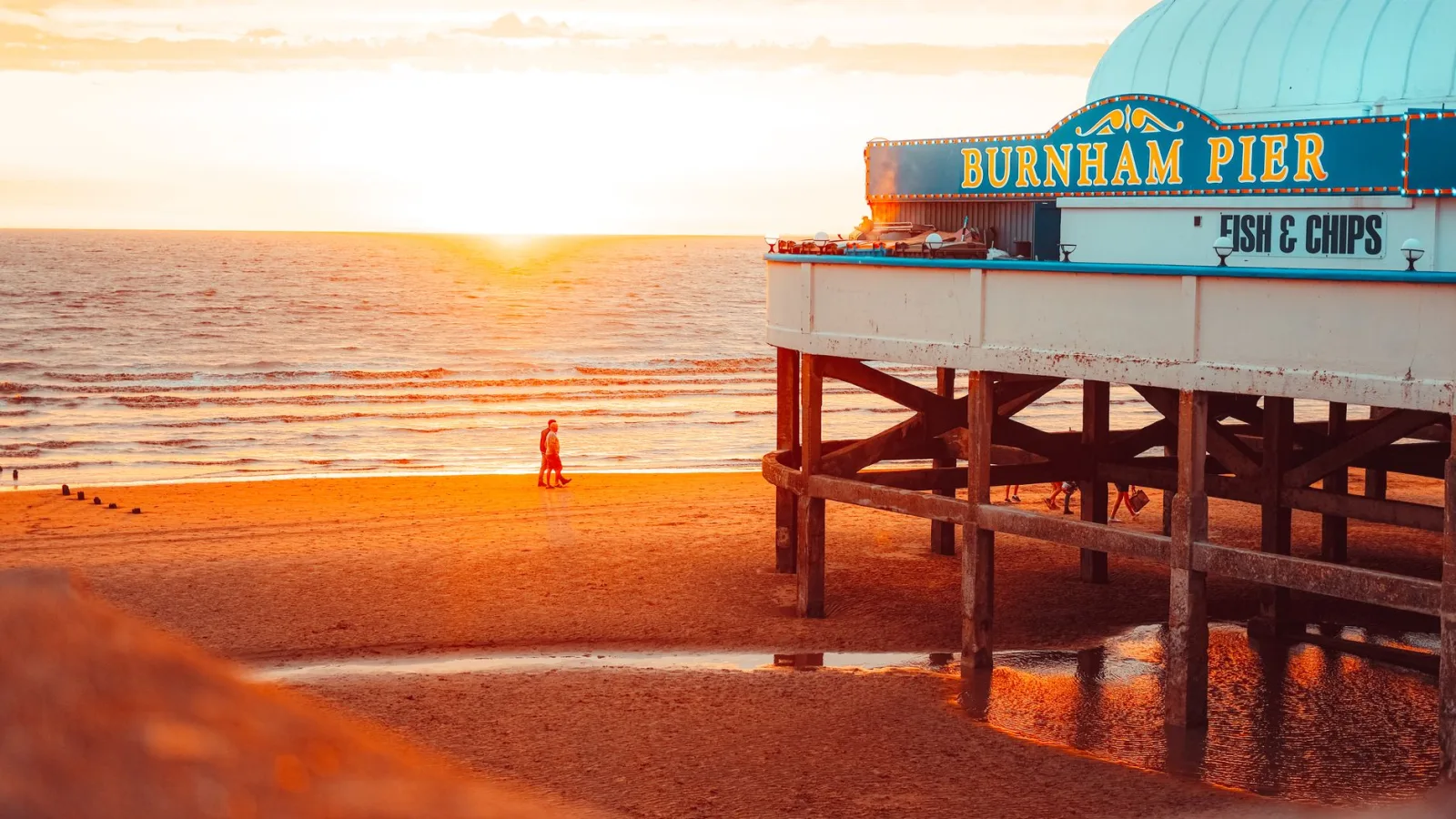 Warm sunset view of Burnham Pier with beachgoers and scenic coastal horizon.