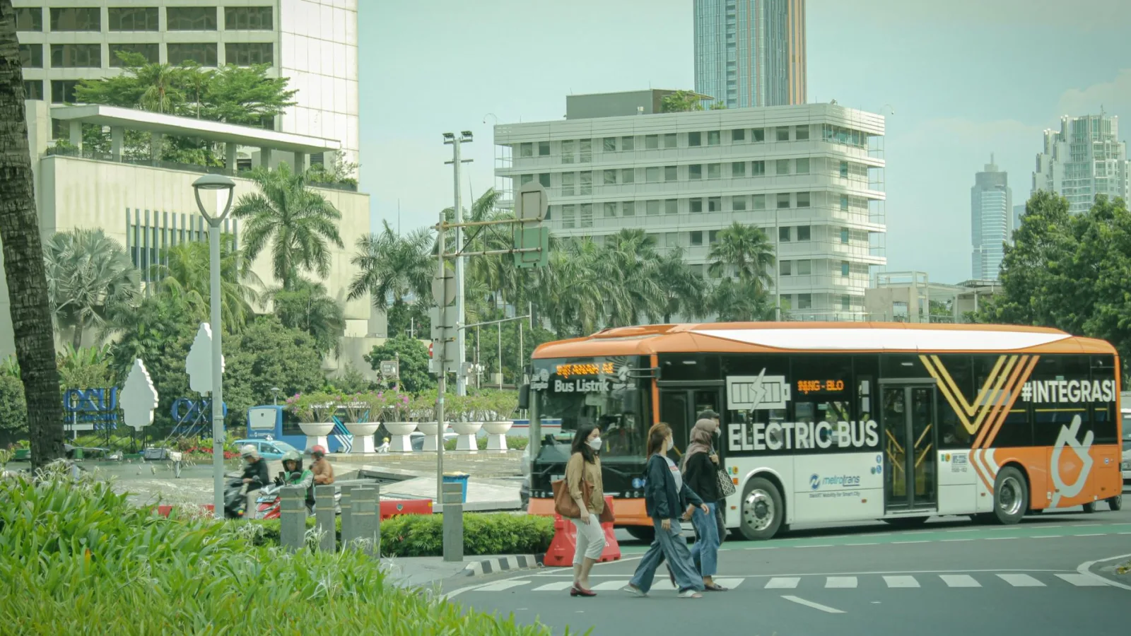 Electric bus on city street in Jakarta, Indonesia amidst urban traffic and pedestrians.