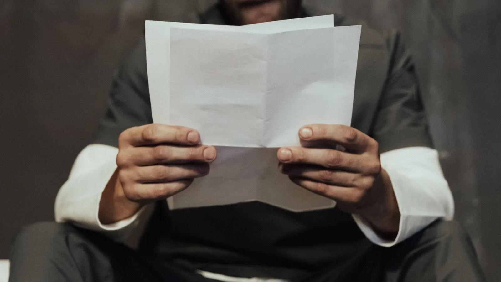 Close-up of a prisoner in uniform reading a letter in a cell setting, highlighting prison life.