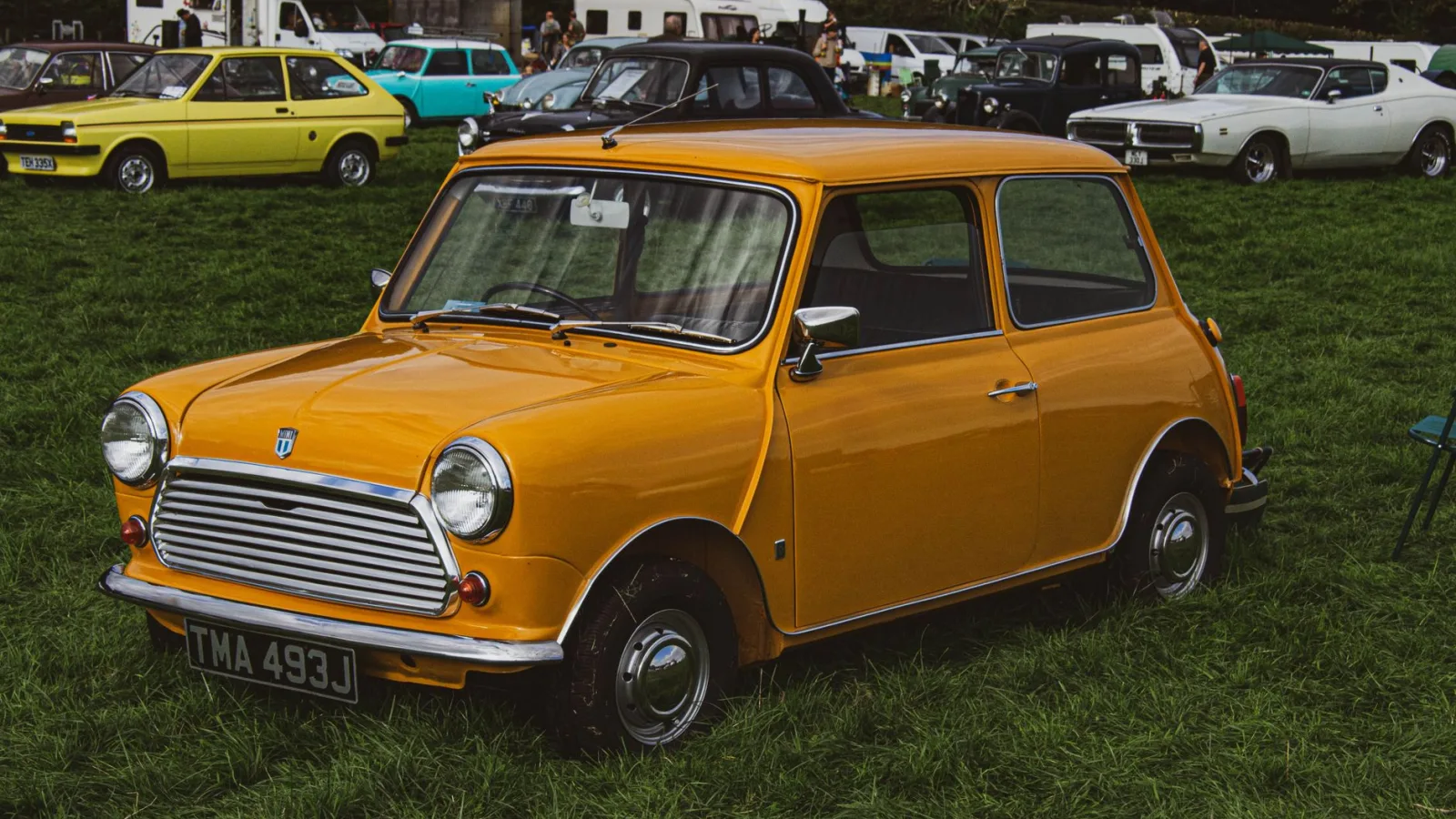 Bright orange vintage Mini car showcased at an outdoor car rally on a grassy field.