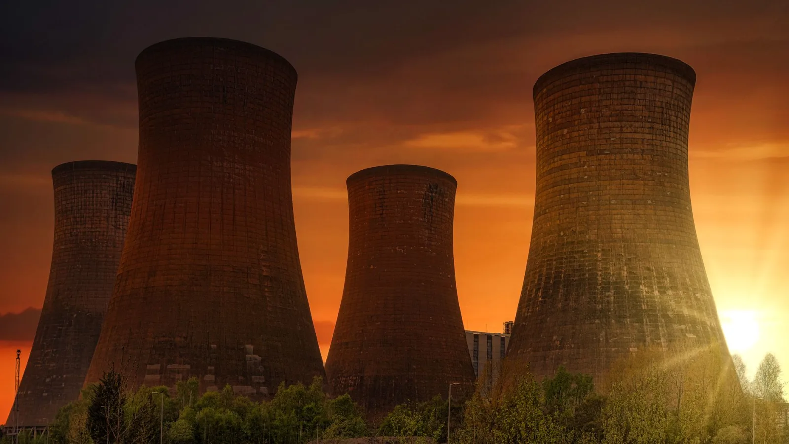 Exterior of huge cooling towers located in contemporary atomic power plant against bright setting sun under dramatic dark sky