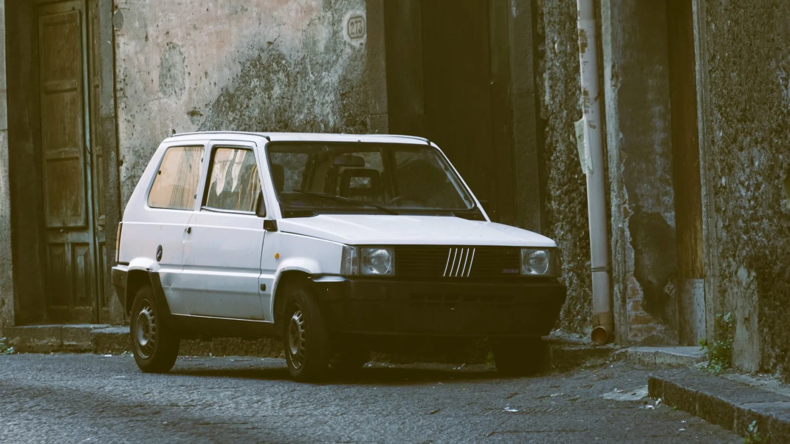 A classic white Fiat Panda parked in a narrow urban alley with vintage charm.