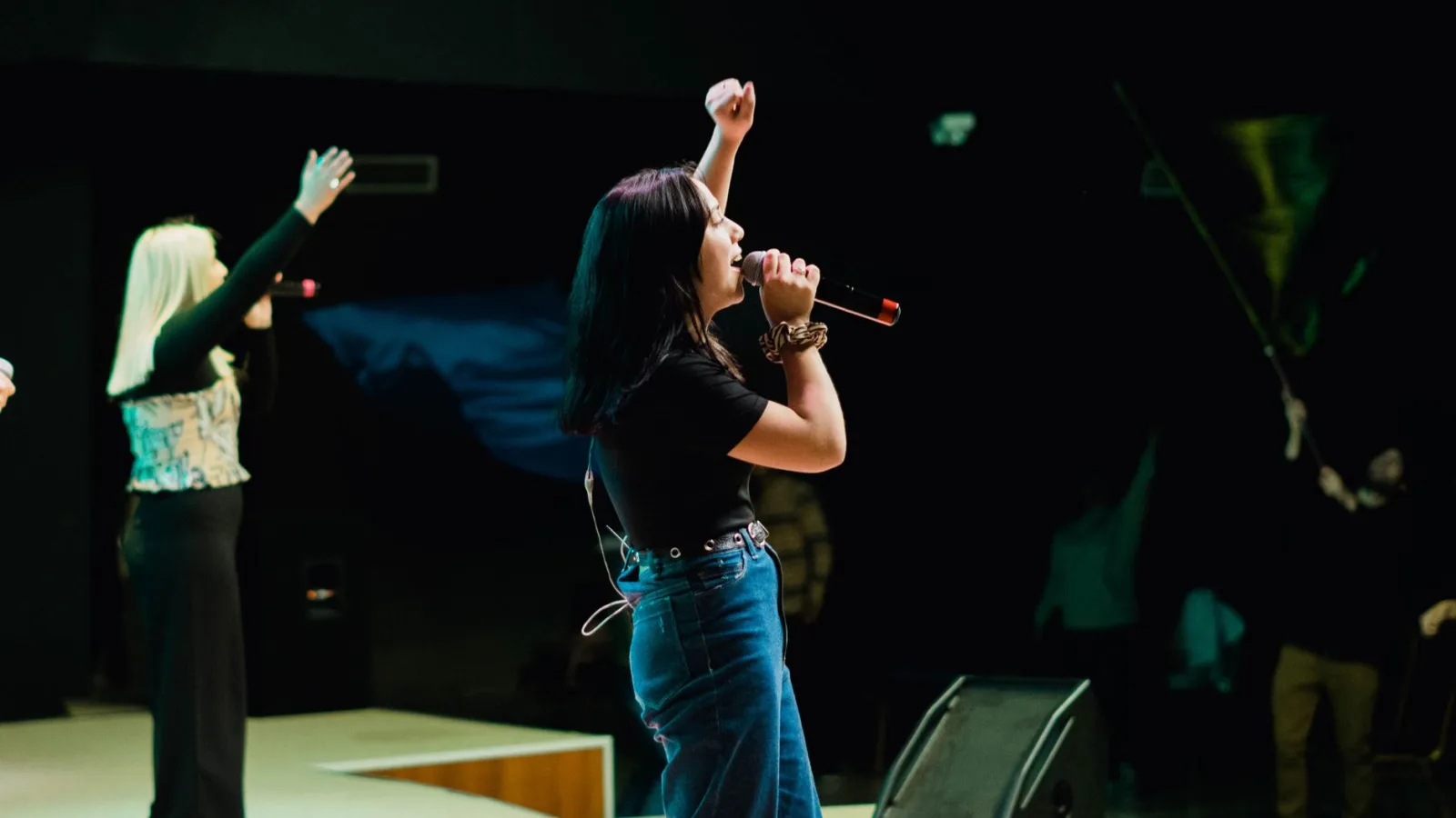 Energetic female musician singing live on stage with arm raised in front of an audience.