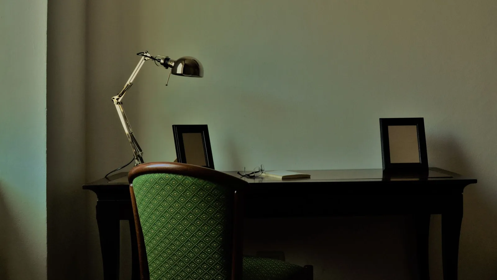 Serene workspace featuring a vintage desk, lamp, and green upholstered chair.