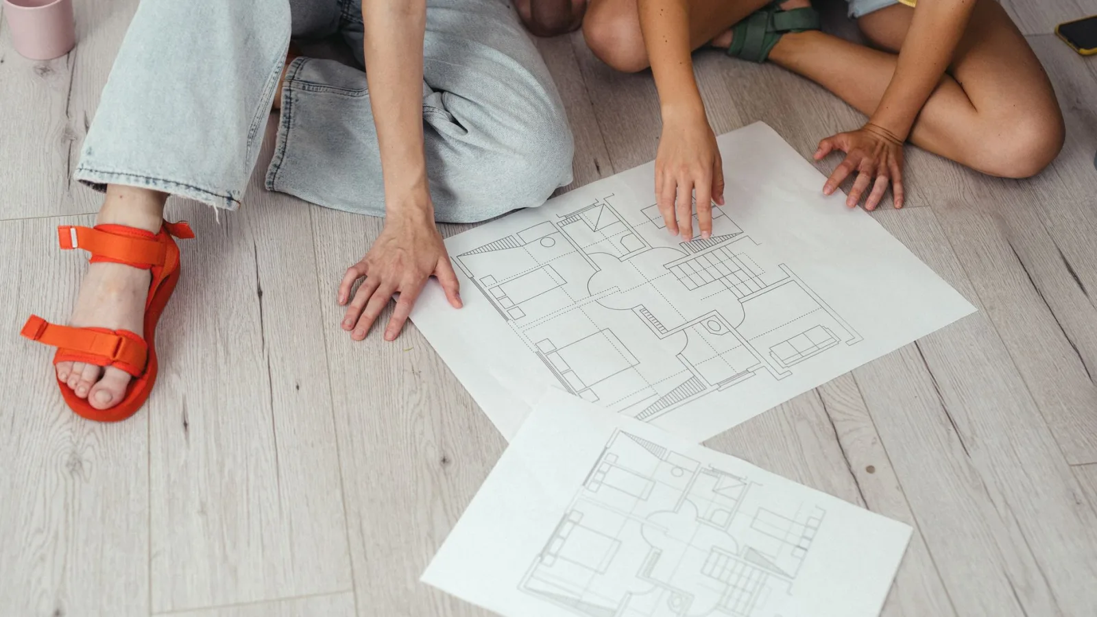 Two people discussing house blueprints on a light wooden floor.