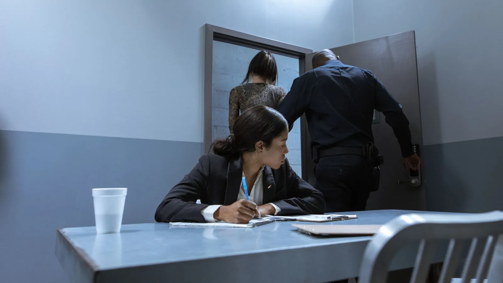 Police officer escorting suspect as lawyer observes during interrogation.