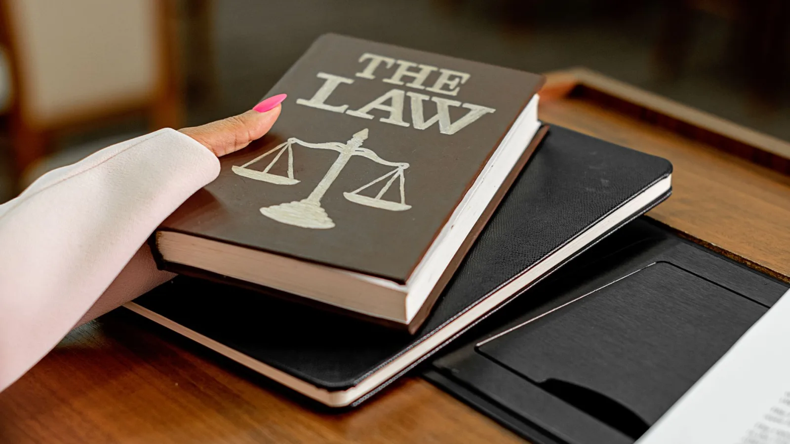 Closeup image of a law book titled 'The Law' on a wooden desk with scales of justice.