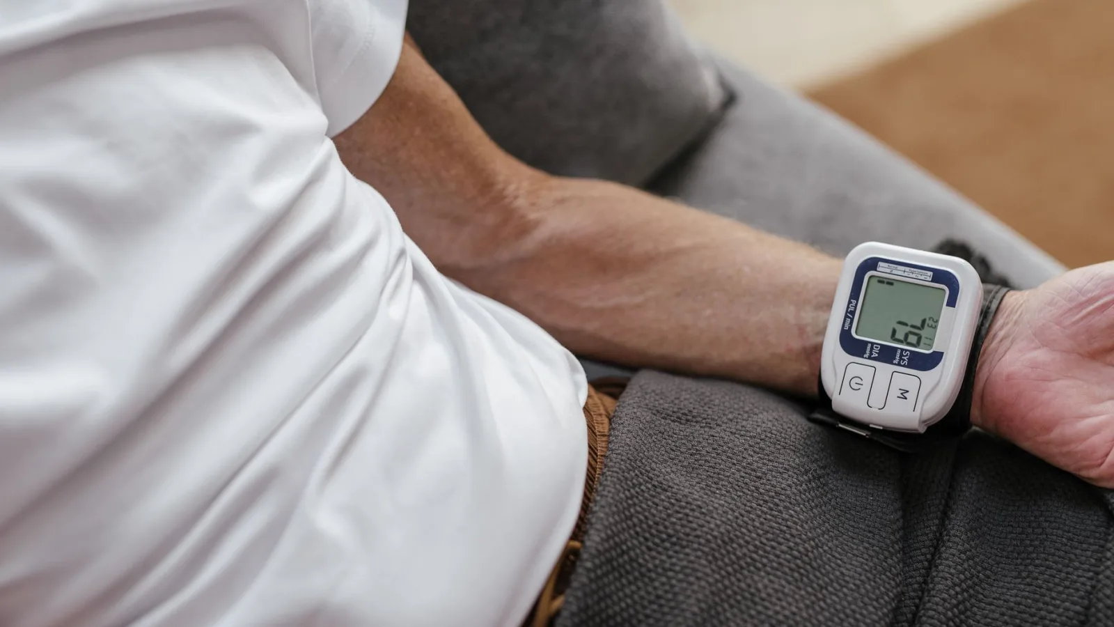 Adult man using a wrist blood pressure monitor to measure blood pressure at home.