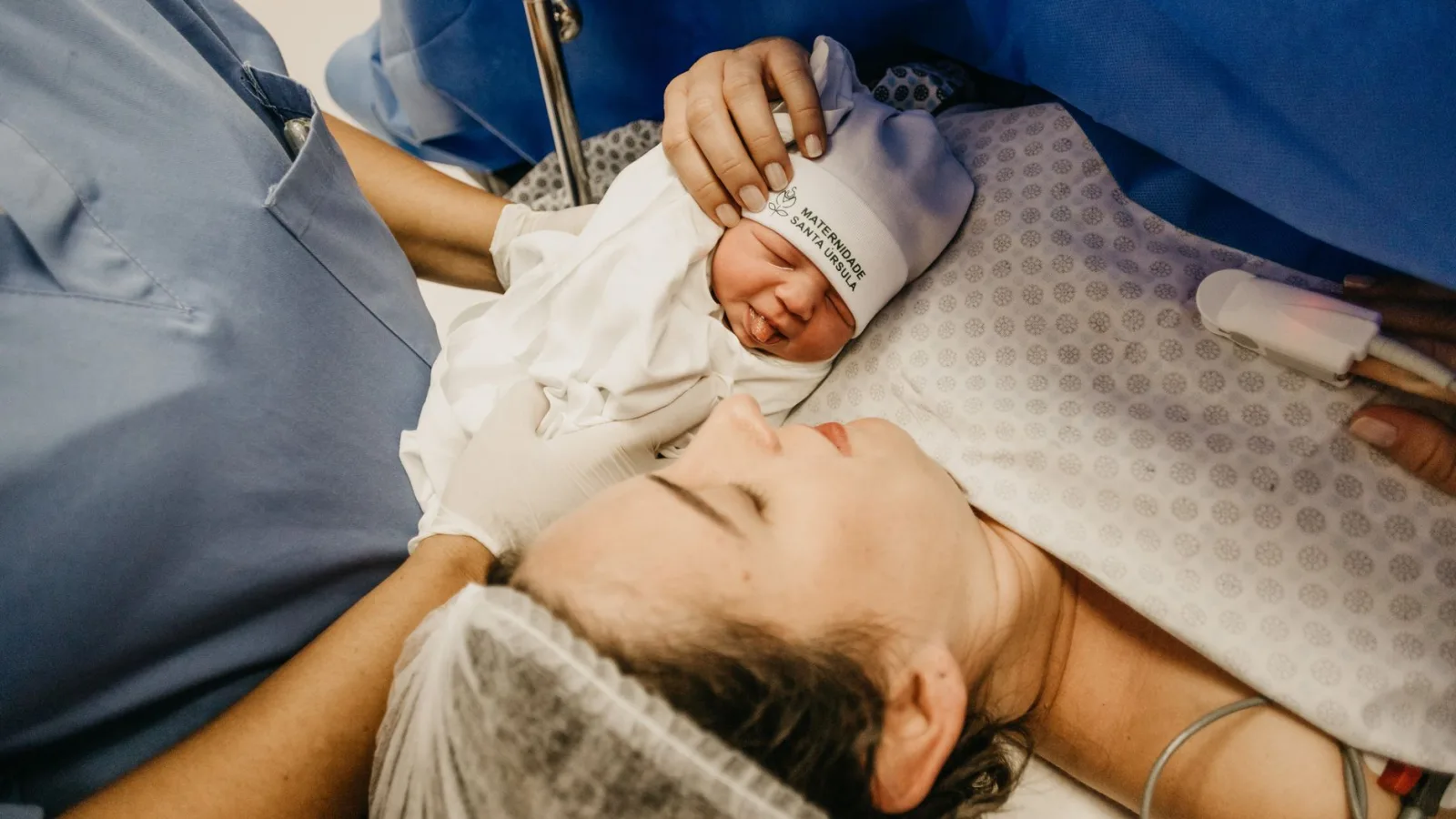 A mother cradling her newborn immediately after childbirth in a hospital setting.