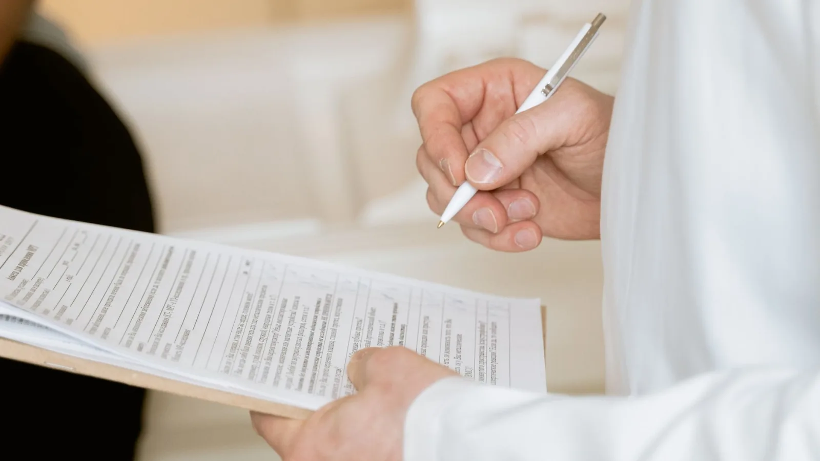 A medical professional in a white coat examines a clipboard with patient documents.