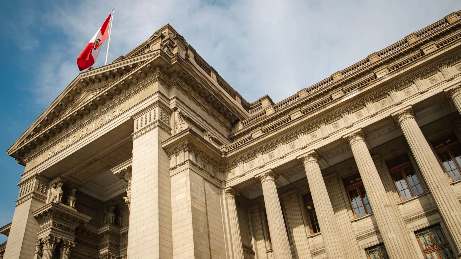 Grand neoclassical government building with Peruvian flag in Lima, Peru, under blue sky.