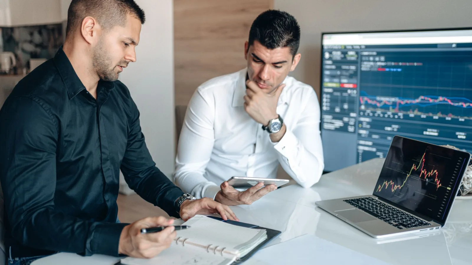 Two businessmen discussing stock market analytics in a modern office setting.