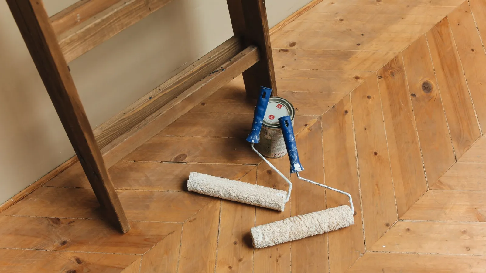 Paint rollers and ladder on a wooden floor, perfect for DIY renovation projects.