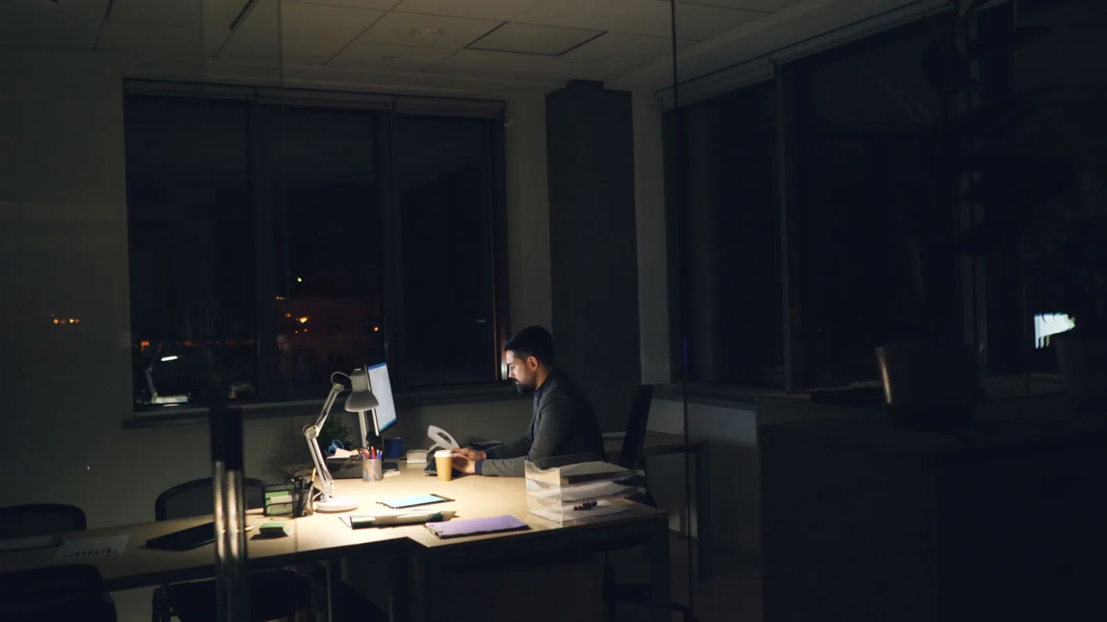 A man working late at night in an office, illuminated by desk light.