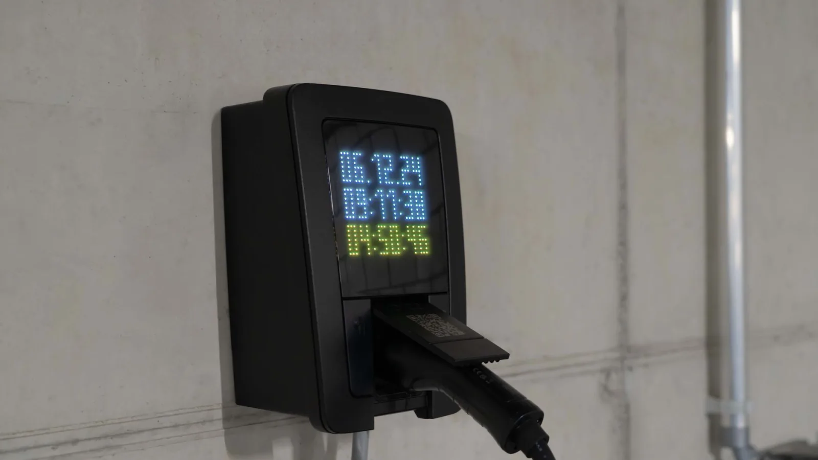 Close-up of an electric car charging station with digital display showing charge stats.