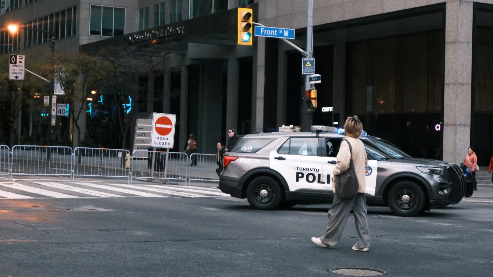 A woman crosses a city street with a Toronto police vehicle nearby.