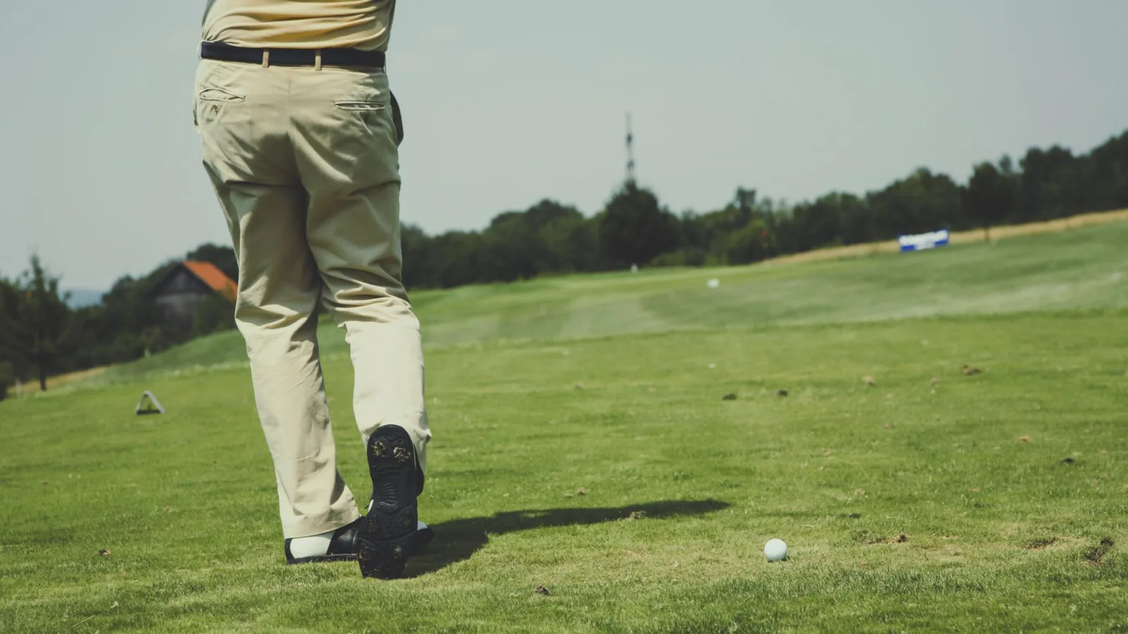 Golfer taking a swing on a sunny day, showcasing leisure and sport on a lush golf course.
