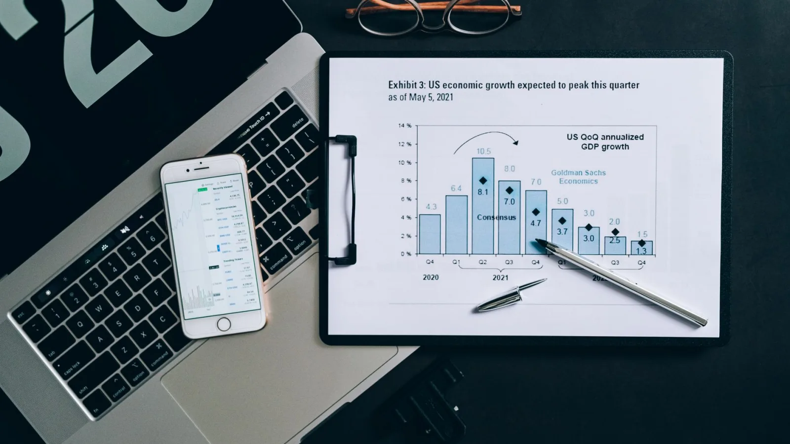 Top view of a financial data analysis setup with laptop, smartphone, and graph on clipboard.