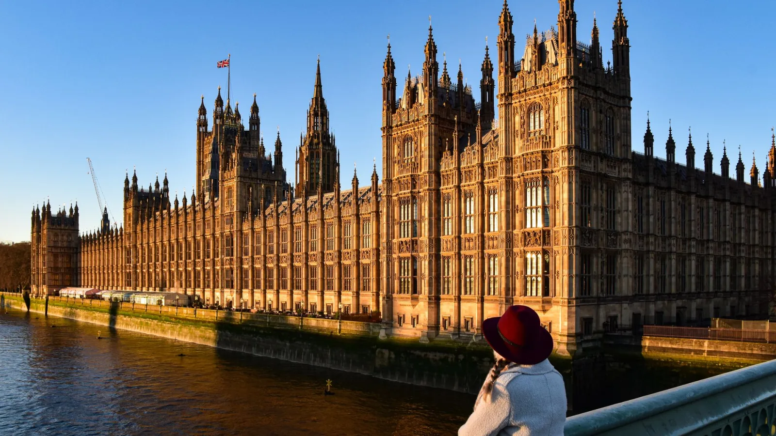 Photograph of Westminster Palace with a person enjoying the view from Westminster Bridge at sunset.
