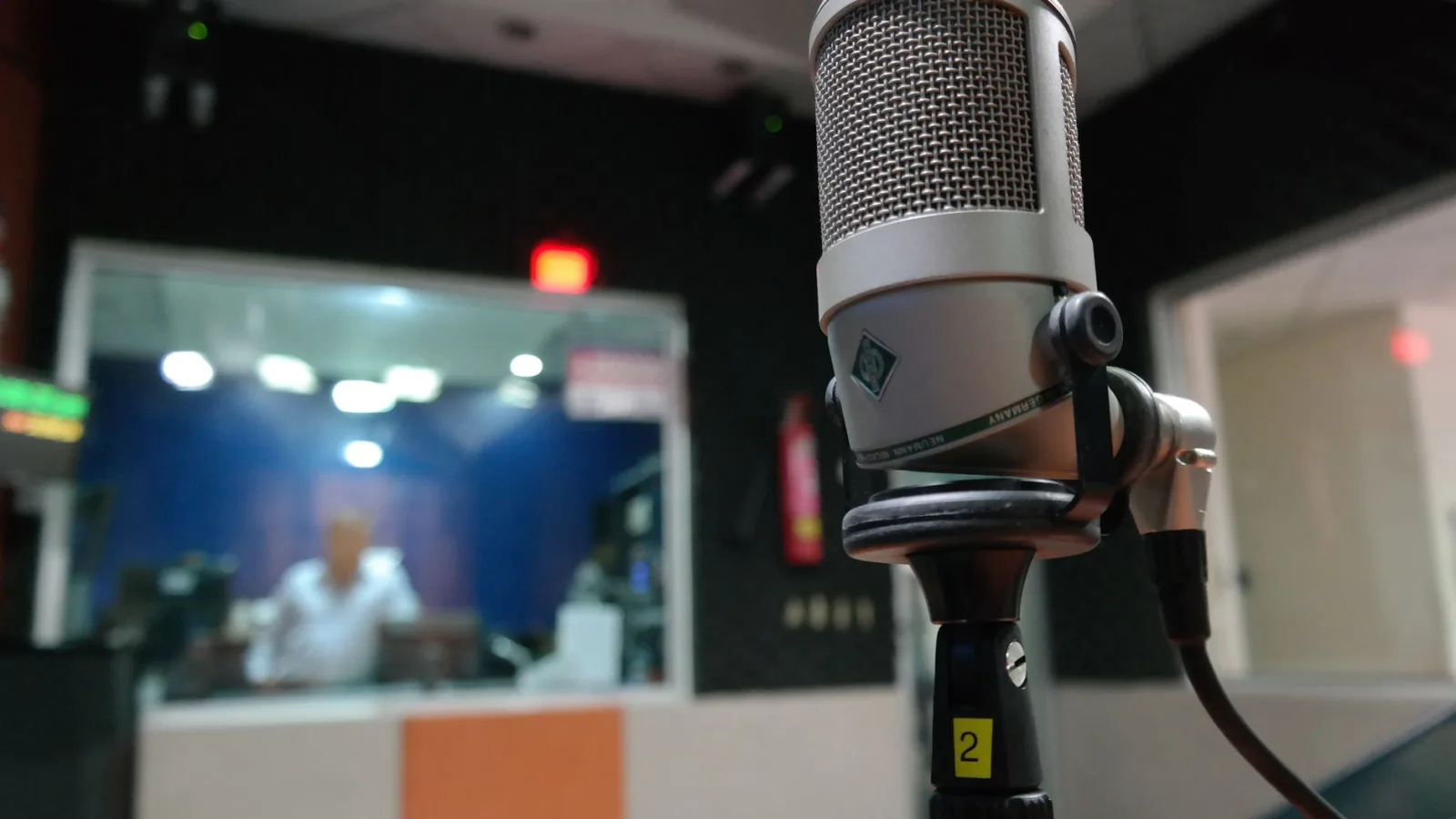 Close-up of a microphone in a recording studio with a blurred sound engineer in the background.