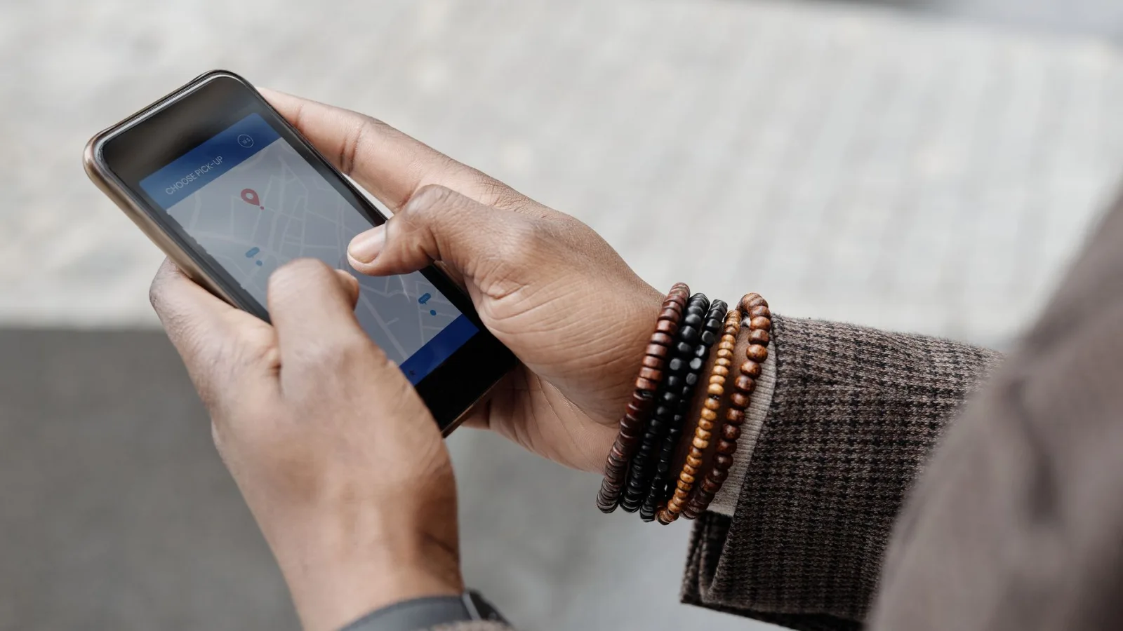 Close-up of hands with bracelets navigating on smartphone using GPS app outdoors.