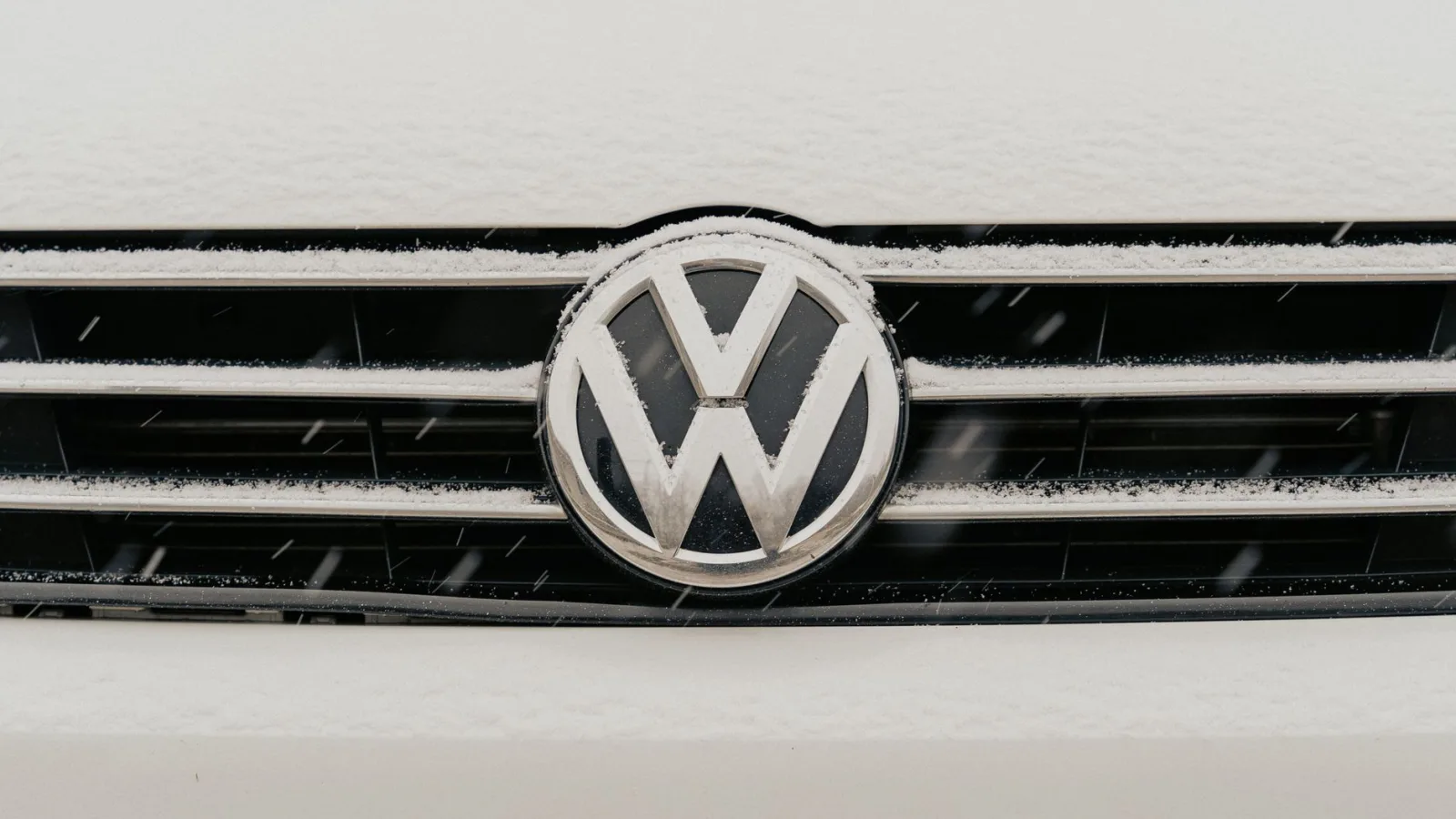 Closeup of a snow-dusted Volkswagen car grille shows the iconic VW logo.